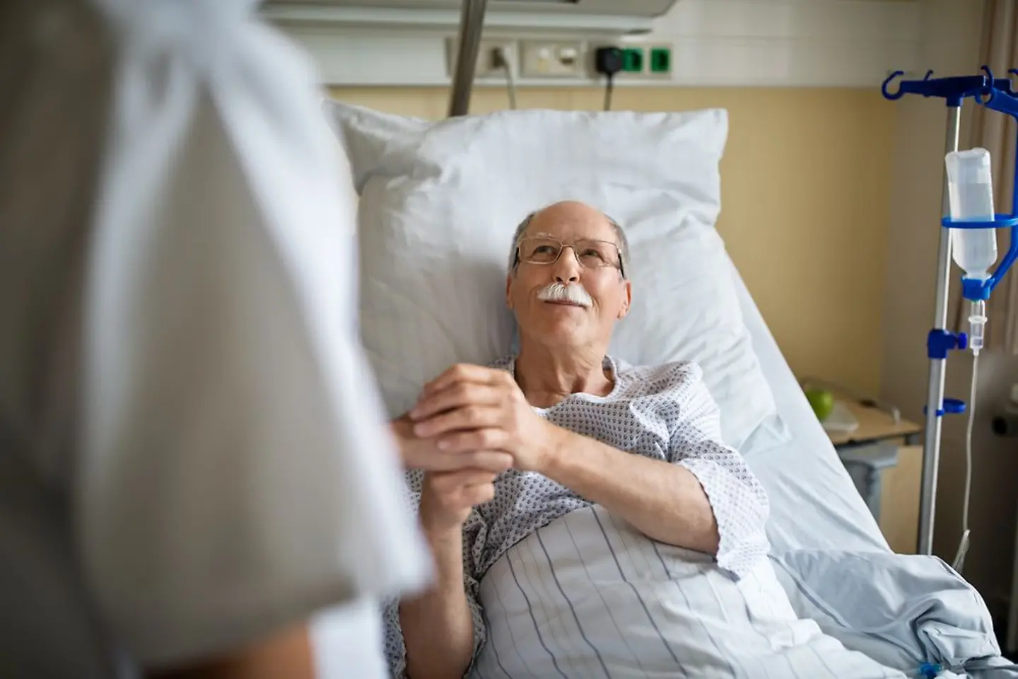Hombre mayor sosteniendo la mano de una enfermera en la habitación del hospital.