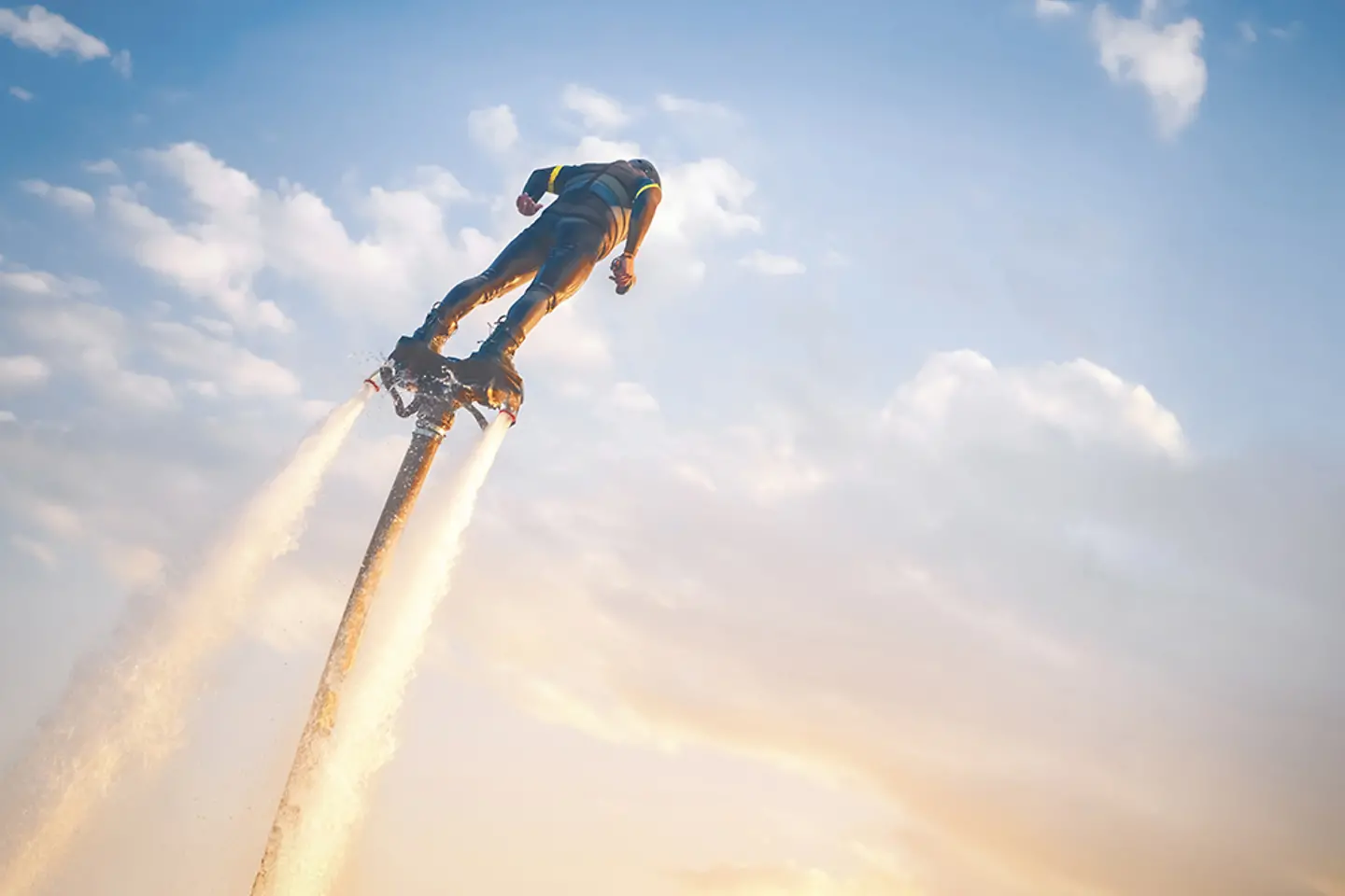 Ein Flyboarder schwebt vor dem Hintergrund eines Sonnenuntergangs über dem Wasser, getragen von kraftvollen Wasserstrahlen.