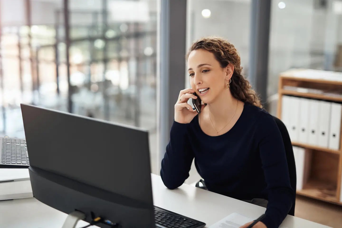 Young woman sits at her laptop and talks on the phone.