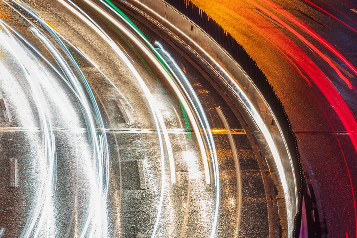 Kurve einer mehrspurigen Straße bei Nacht, die Lichter der Autos bilden leuchtende Linien, die Autos sind nicht erkennbar 