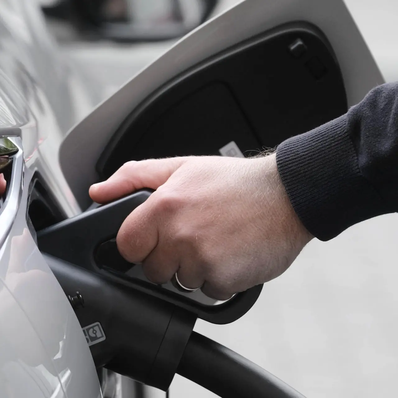 A hand holds a charging cable that is plugged into a car