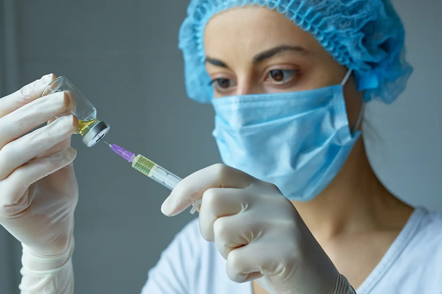 Nurse with mask and gloves, preparing for injection, with a syringe with liquid vaccine
