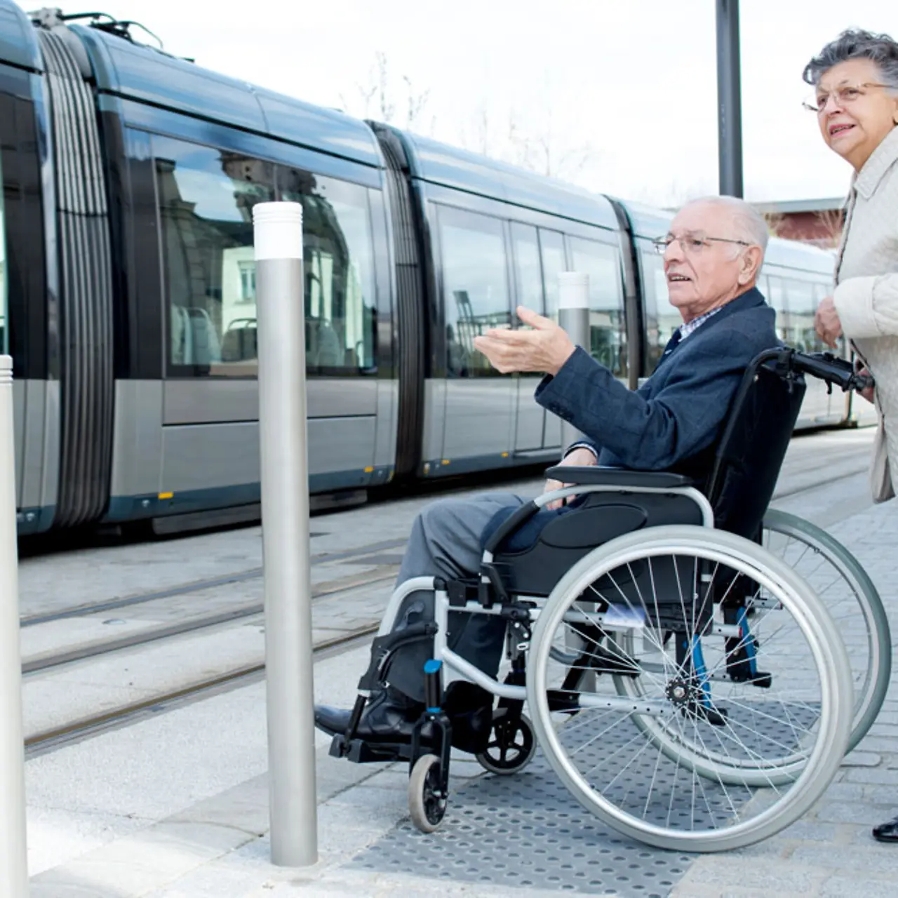 Pareja de ancianos esperando el tren en silla de ruedas, infraestructura de transporte público