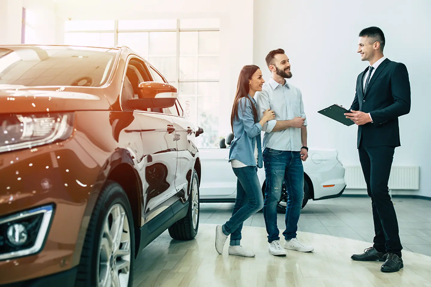 A young couple at a car dealership, talking with a salesman.